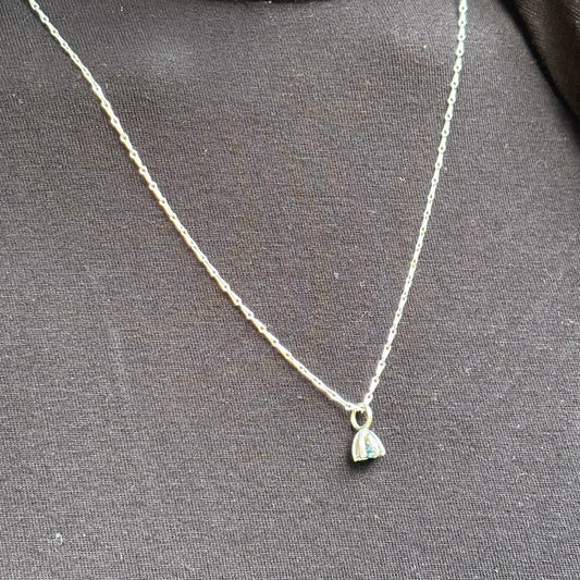 A delicate silver chain necklace with a small silver pendant featuring a light blue stone, displayed on a dark gray textured fabric background.